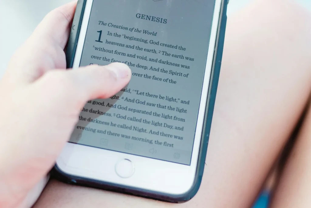 Close-up of a hand holding a smartphone displaying the Bible book Genesis on screen.