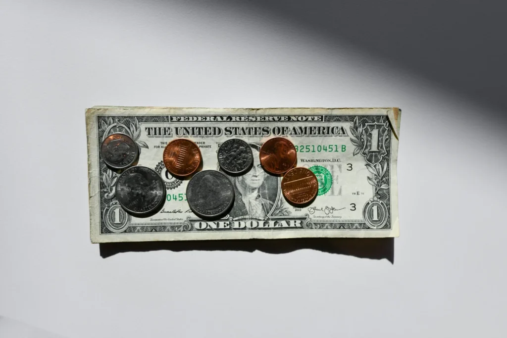 One-dollar bill with a mix of pennies, nickels, and dimes laid on top on a white surface
